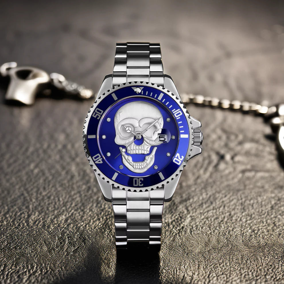 L'Orologio con teschio 3D silver blue di PACOSHOP, caratterizzato da un sorprendente design a teschio e da una lunetta blu, poggia su una superficie strutturata con una catena e una chiusura metalliche sfocate visibili sullo sfondo.