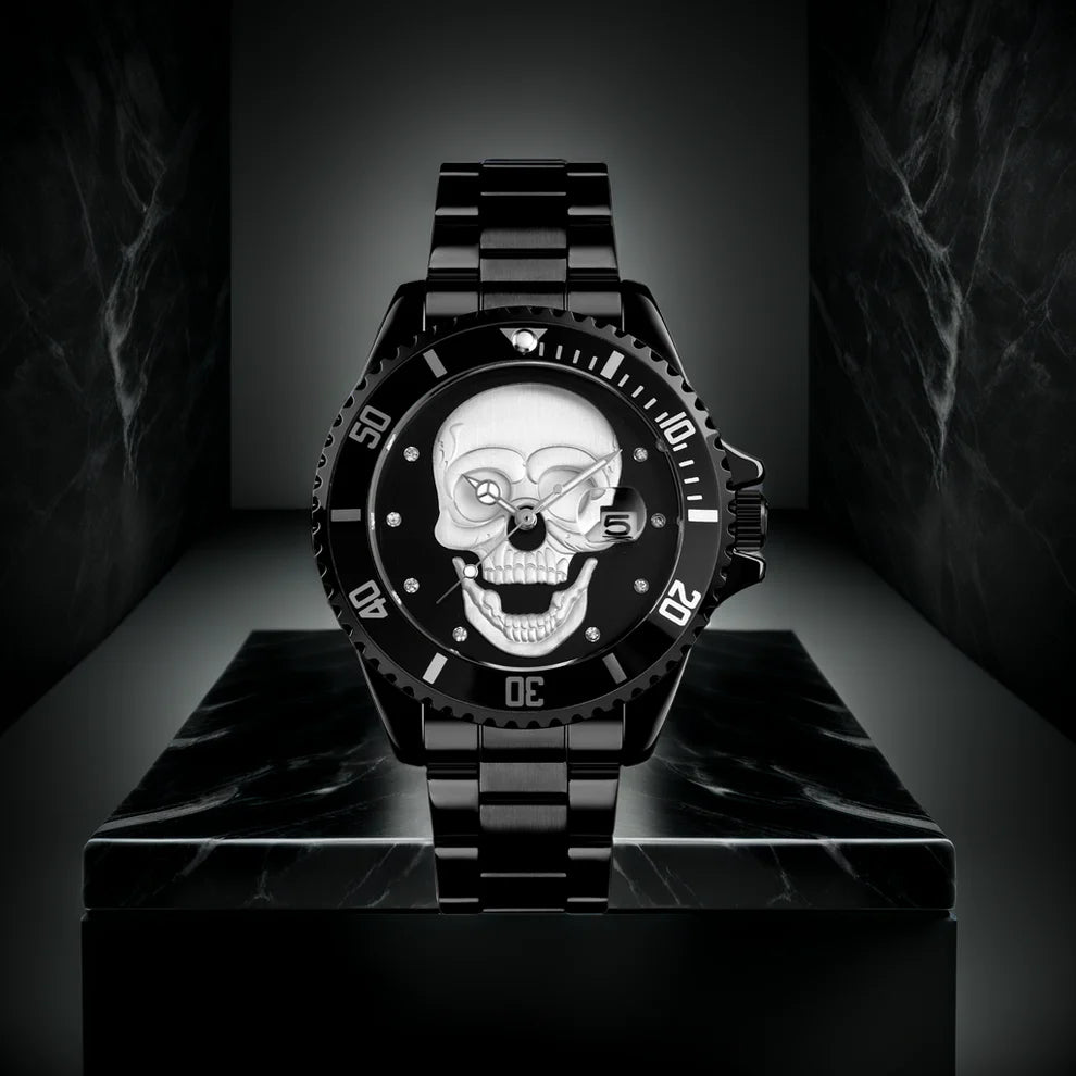 L'Orologio con teschio 3D All Black di PACOSHOP, caratterizzato da un cinturino in metallo e da un teschio argentato con un occhio di pietra preziosa sul quadrante, è esposto su un piedistallo di marmo nero su uno sfondo scuro.