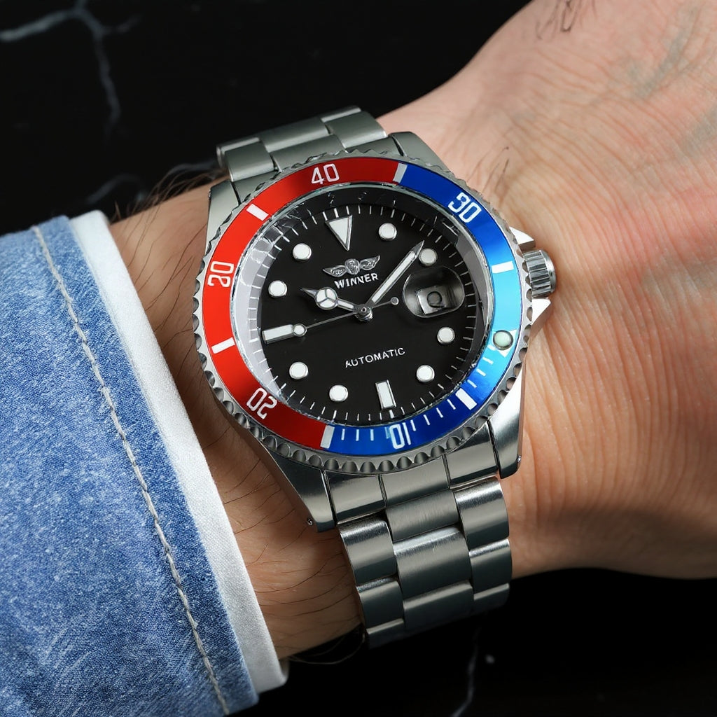 Un PACOSHOP24.COM Orologio automatico uomo meccanico mod. Gmt con lunetta rossa e blu, quadrante nero e bracciale in metallo, indossato al polso di una persona. Il quadrante dell'orologio riporta il marchio PACOSHOP24.COM e la dicitura "Automatic".