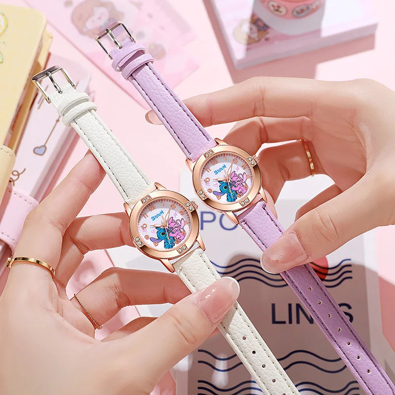 Due mani reggono gli orologi Orologio bambini cartoon Stitch di PACOSHOP24.COM: uno con cinturino bianco, l'altro color lavanda. Entrambi con cassa in oro, sono circondati da articoli di cancelleria e accessori color pastello per un look giocoso.