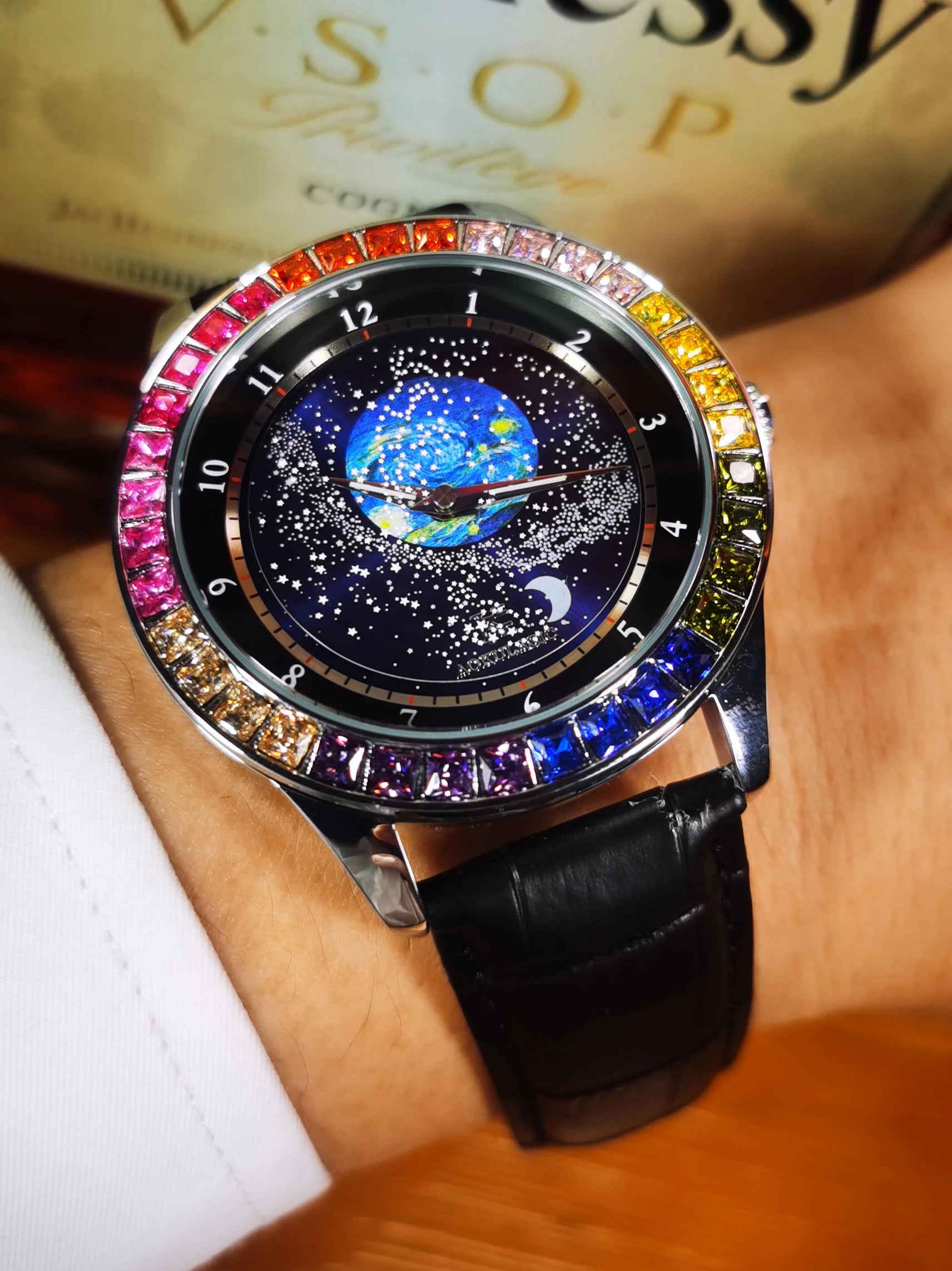 L'Orologio automatico uomo cielo stellato Design luminoso di PACOSHOP24.COM presenta una lunetta con pietre preziose colorate e un quadrante a tema galattico - Terra blu, stelle bianche e luna crescente - abbinato a un cinturino in pelle nera per un look davvero accattivante.