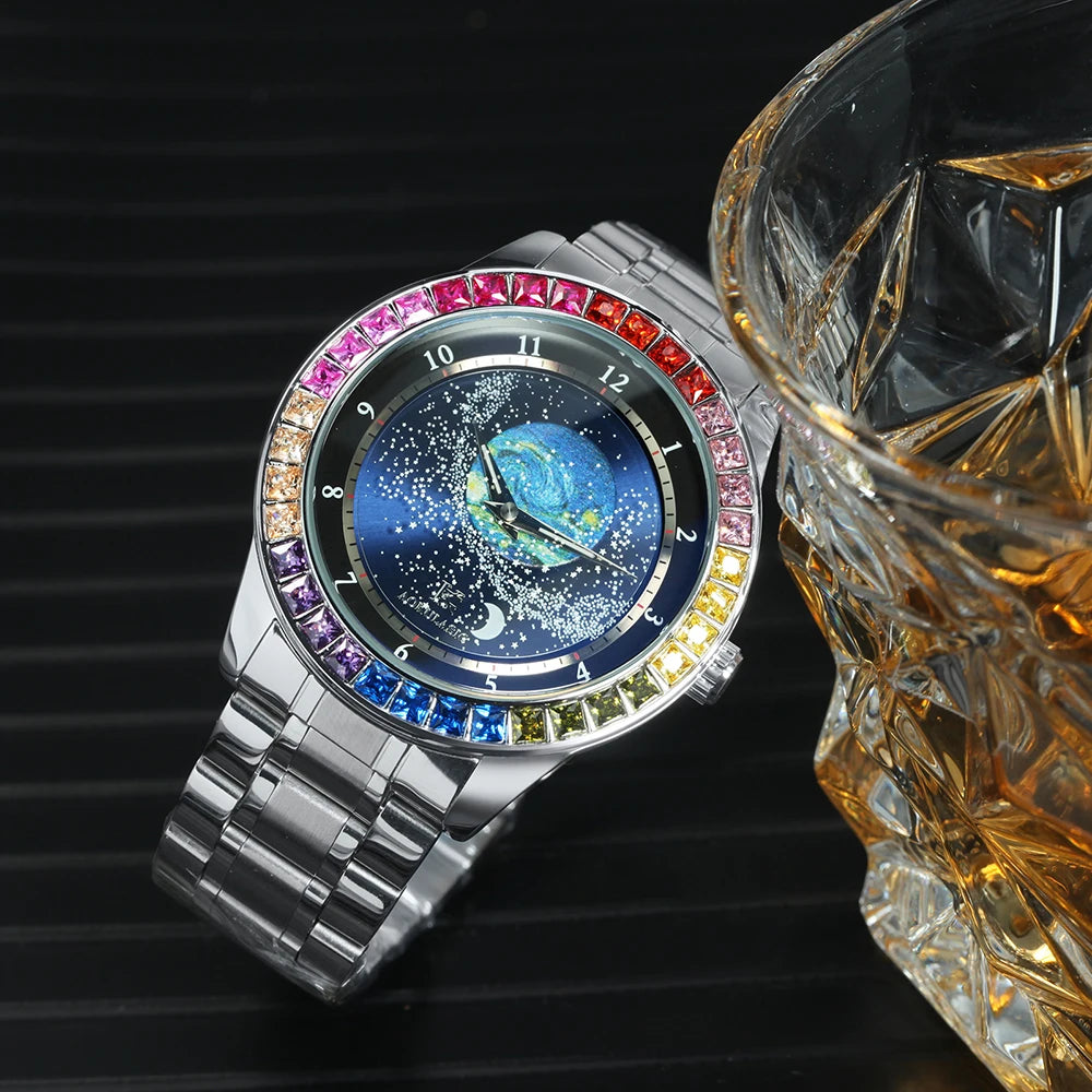 L'Orologio automatico uomo cielo stellato Design luminoso di PACOSHOP24.COM presenta una cassa argentata, un quadrante blu stellato e una lunetta con pietre preziose multicolori, affiancata da un bicchiere sfaccettato di bevanda ambrata su una superficie scura a righe.