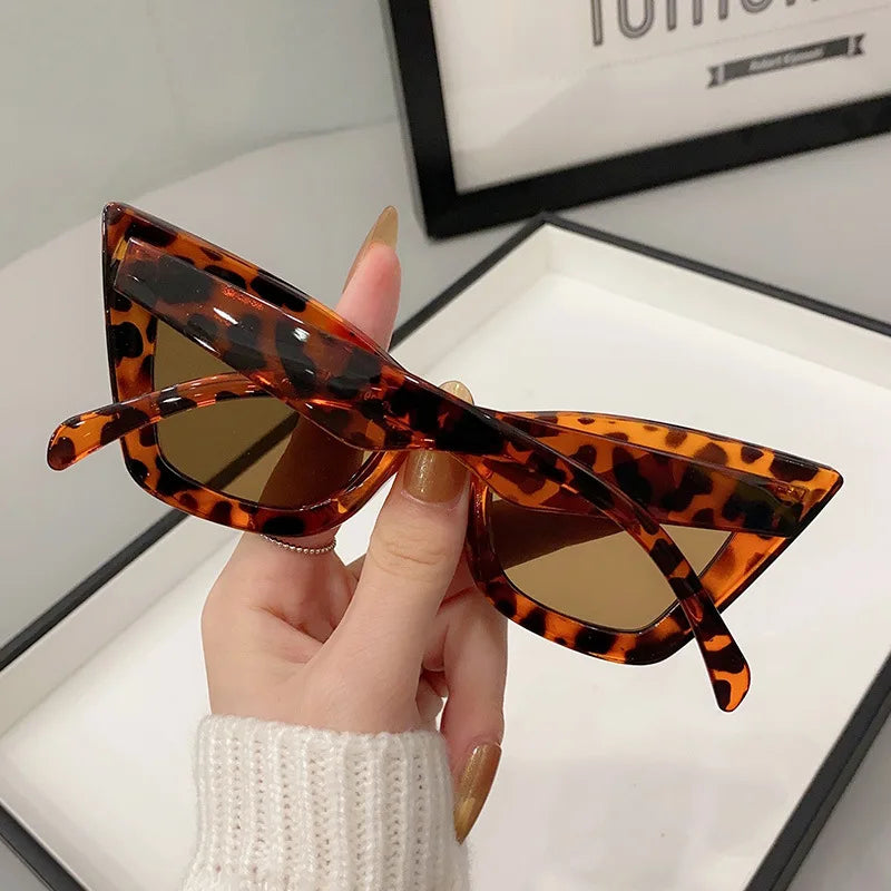 Una mano con unghie curate regge PACOSHOP24.COM Occhiali da Sole Donna Occhi di Gatto - Fashion Style, caratterizzati da un audace motivo tartarugato e lenti marroni, perfetti per un look chic e moderno.