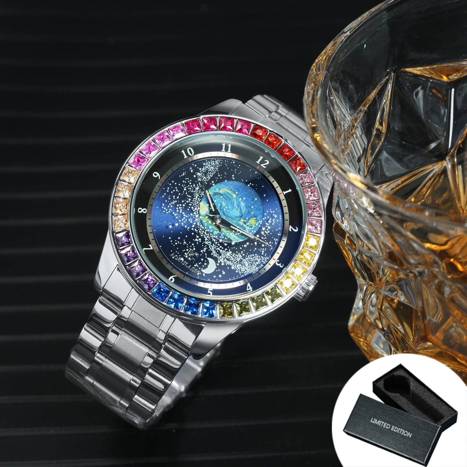 L'Orologio automatico uomo cielo stellato Design luminoso di PACOSHOP24.COM, caratterizzato da lunetta con pietre preziose, quadrante blu celeste e fasi lunari, si trova accanto a un bicchiere di liquido ambrato. Nell'angolo è esposta una scatola nera LIMITED EDITION aperta.