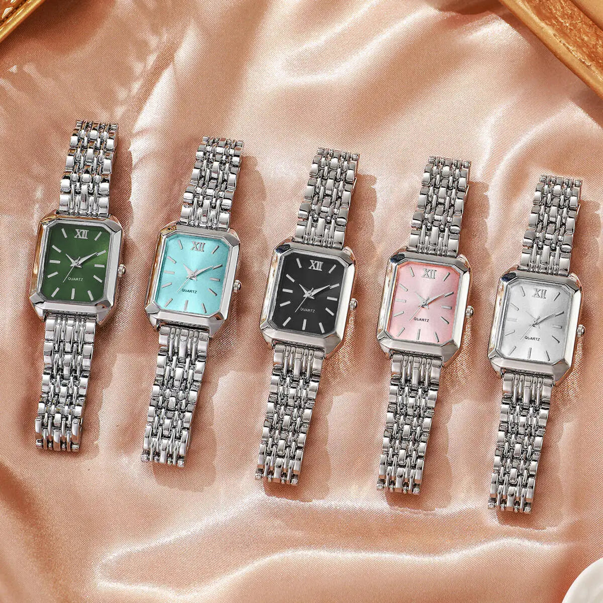 Cinque orologi da polso in argento PACOSHOP24.COM Orologio al quarzo donna rettangolare alla moda & Fashion, con quadranti verdi, blu, neri, rosa e bianchi, sono esposti uno accanto all'altro su un tessuto di raso beige lucido.