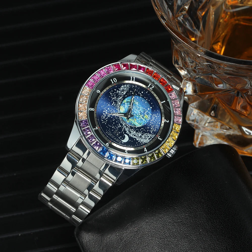 L'Orologio automatico uomo cielo stellato Design luminoso di PACOSHOP24.COM, con cassa argentata, lunetta con gemme colorate e quadrante notturno stellato, poggia su una superficie nera accanto a un vetro sfaccettato di liquido ambrato.