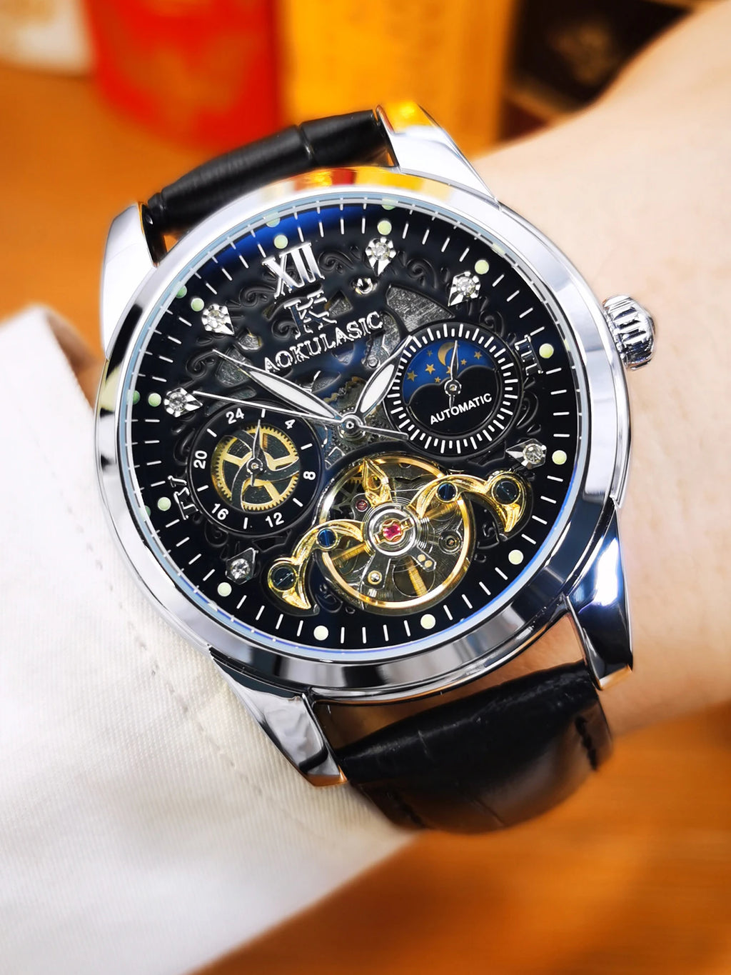 Un primo piano dell'Orologio automatico scheletrato uomo Tourbillon Design di PACOSHOP24.COM mostra il cinturino in pelle nera, la cassa argentata e l'intricato quadrante scheletrato con ingranaggi a vista, numeri romani e contatori multipli.
