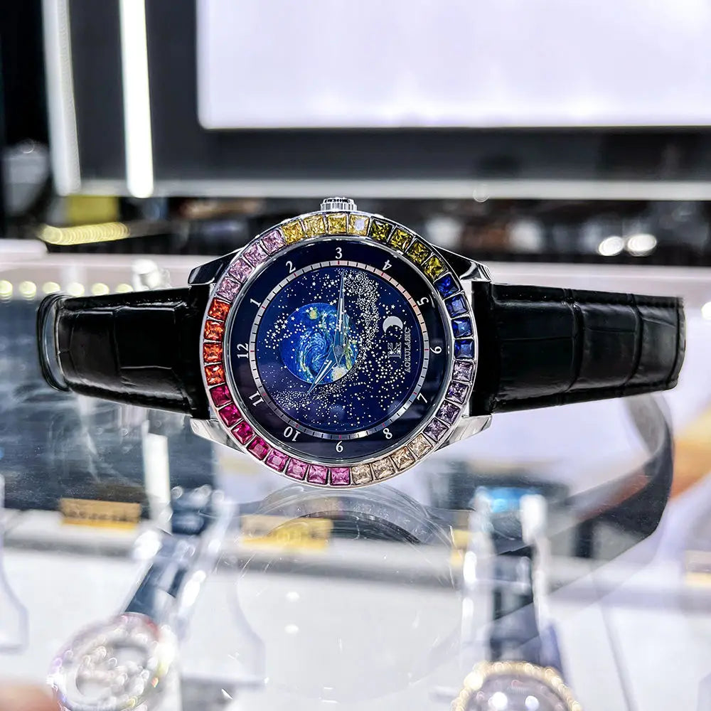 L'Orologio automatico uomo cielo stellato di PACOSHOP24.COM presenta un lussuoso cinturino in pelle nera, una lunetta con gemme arcobaleno e un luminoso quadrante stellato blu scuro con costellazioni in oro, elegantemente esposto su un supporto trasparente.