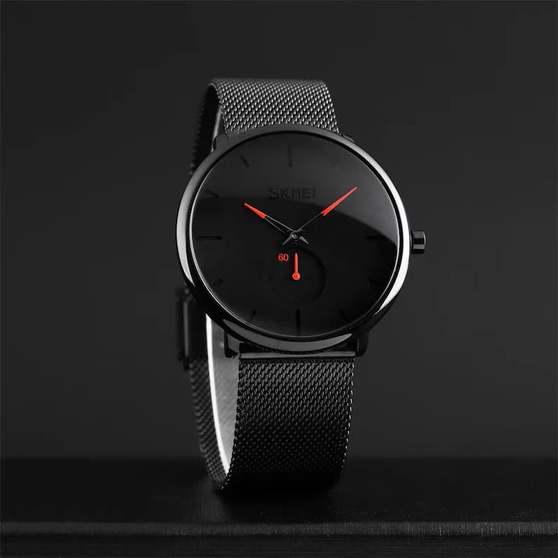 Lo Skmei Orologio minimalista ultraleggero ultrasottile nero rosso presenta un elegante cinturino in maglia nera, lancette rosse e una sottile incisione del marchio: un elegante orologio in acciaio inossidabile che spicca su qualsiasi sfondo scuro.