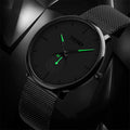 Lo Skmei Orologio minimalista ultraleggero ultrasottile nero verde presenta un elegante cinturino in maglia, un quadrante minimalista e lancette verdi luminose, su uno sfondo geometrico scuro.