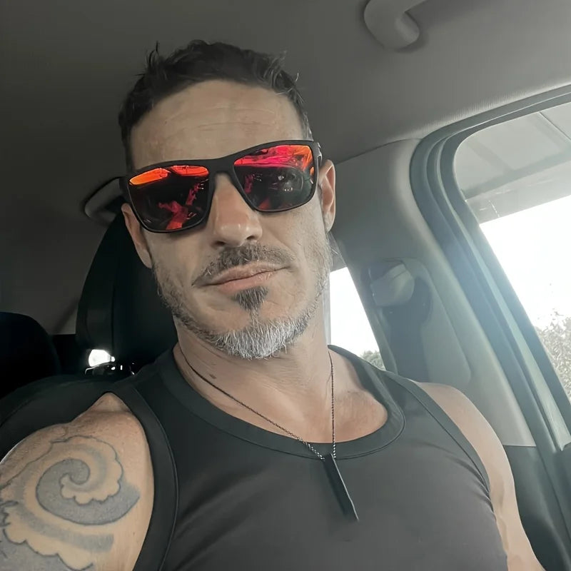Un uomo con capelli corti e scuri e pizzetto sale e pepe siede in auto e indossa PACOSHOP24.COM occhiali da sole unisex polarizzati a specchio sportivi, una canottiera nera e una collana con ciondolo. Sulla parte superiore del braccio è visibile un tatuaggio.