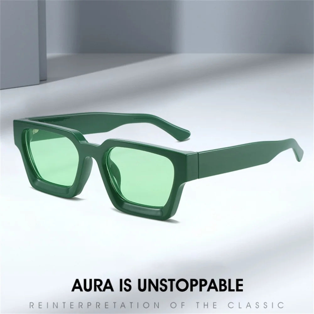 Gli Occhiali da sole con montatura quadrata Fashion Retrò Vintage di PACOSHOP24.COM, con montatura spessa verde e lenti verdi UV400, sono esposti su una superficie bianca. In basso è riportato il testo: AURA IS UNSTOPPABLE - REINTERPRETAZIONE DEL CLASSICO.