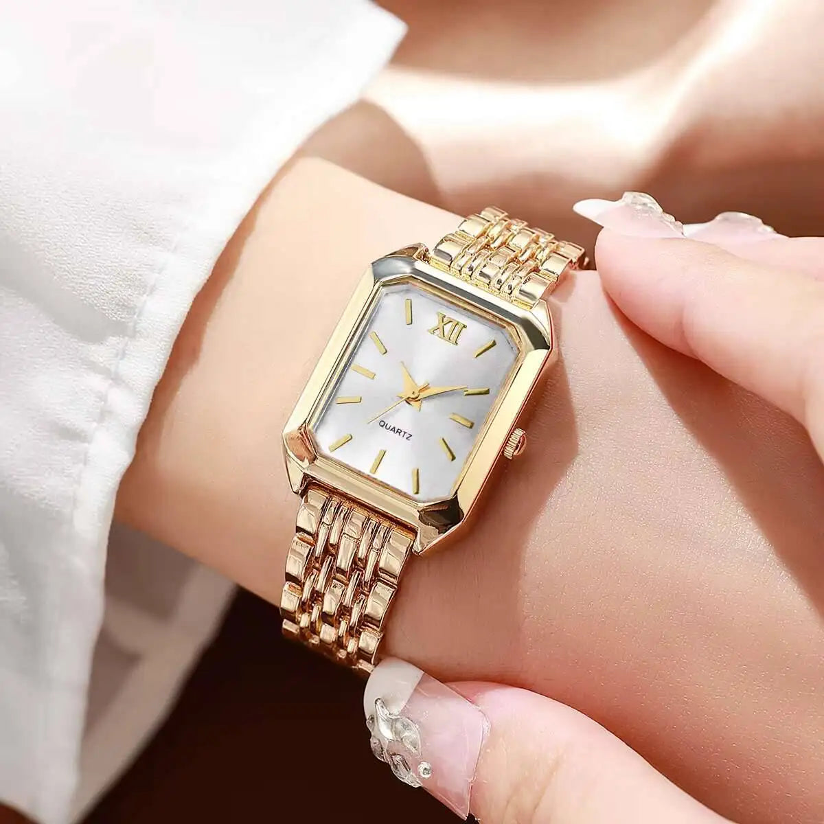 Una donna che indossa il PACOSHOP24.COM Orologio al quarzo donna rettangolare alla moda & Fashion, con fascia a maglie in metallo dorato, quadrante bianco, indici in oro e numero romano XII, si tiene delicatamente il polso con l'altra mano.