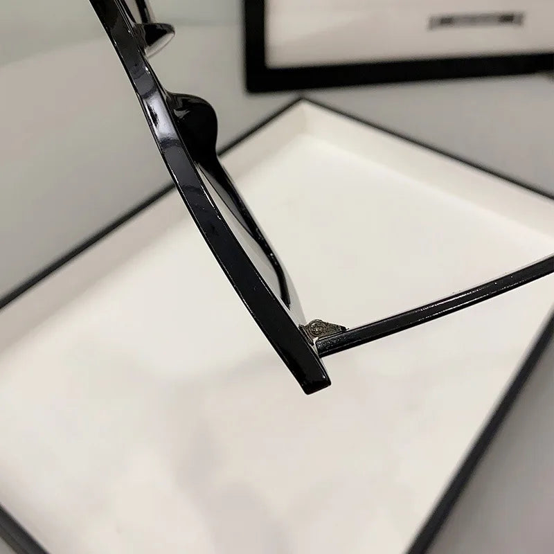 Un primo piano dell'asta e della cerniera di PACOSHOP24.COM Occhiali da Sole Donna Occhi di Gatto - Fashion Style mostra l'elegante montatura nera, con scatola bianca e sfondo sfocato per un look chic.