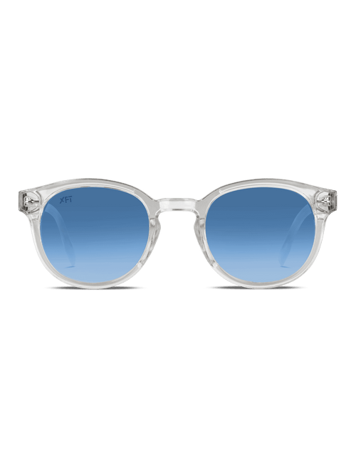 I Luminatrix di X Frame Therapy sono occhiali da sole rotondi unisex con montatura chiara e lenti blu sfumate con protezione UV, su sfondo bianco.