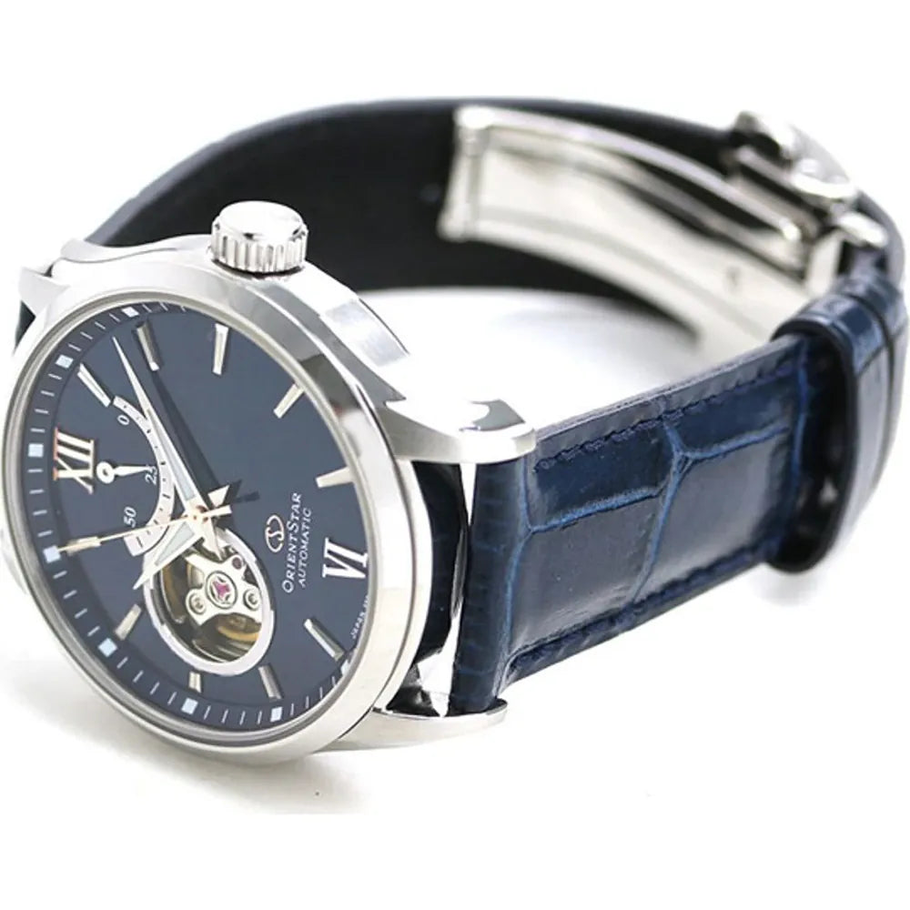 L'Orient Star Open Heart Automatico RE-AT0006L00B di Orient presenta un cinturino in pelle blu, una cassa argentata, un quadrante a numeri romani blu scuro e un display con movimento giapponese a cuore aperto. L'orologio è inclinato per evidenziare l'eleganza del quadrante e della chiusura.